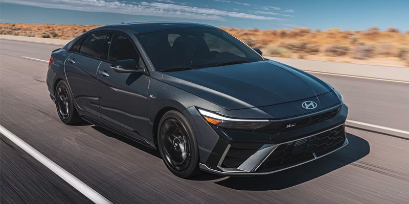 Dark Hyundai Elantra sedan driving on a highway under a sunny sky