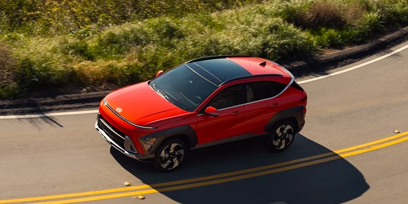 Red Hyundai Kona driving on a winding, sunny road.