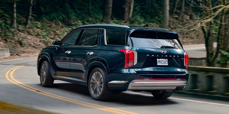 Green Hyundai Palisade SUV driving away on a winding forest road.